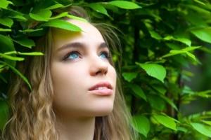 A girl standing around leaves and looking up.