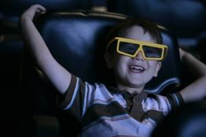 A young boy smiling at a movie theater with 3d glasses.