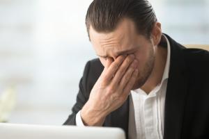 A business man with eye fatigue while looking at a laptop.