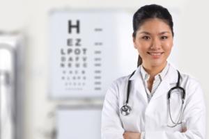 An optometrist smiling in front of an eye chart.