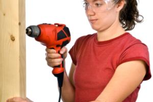 A woman holding a drill and using eye goggles.