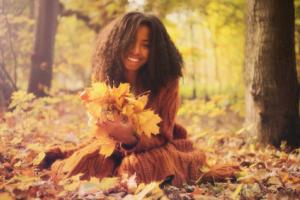 A girl smiling outdoors and holding autumn leaves.