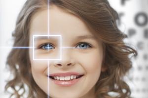 A young kid with contact lenses in front of a blurry eye chart.