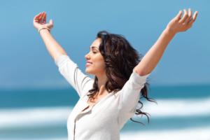 A women smiling with her arms up at the beach.