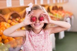 A young girl holding strawberries in front of her eyes at a market.