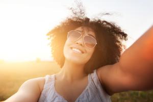 A woman smiling and wearing sunglasses outdoors.