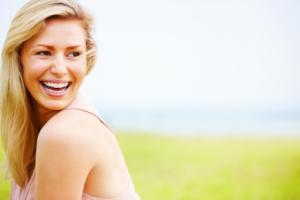 A woman smiling outdoors in an open field.