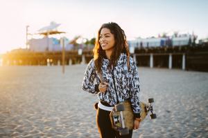 A woman smiling and holding a skateboard on the beach.