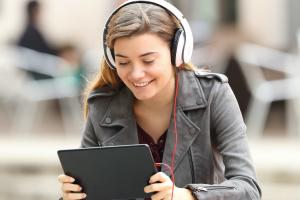 young woman wearing headphones and smiling at a tablet. 