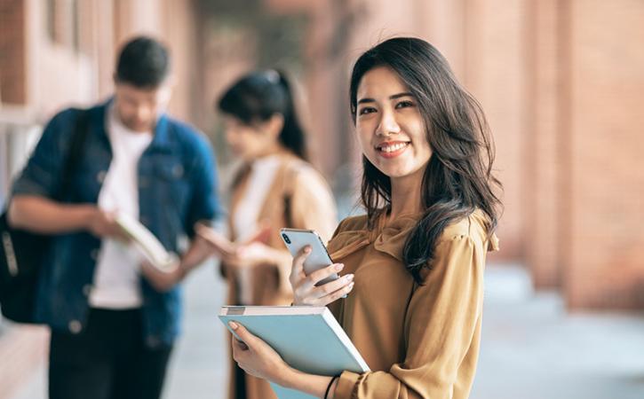 Student smiling and holding notebook and smartphone.