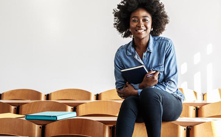 College student holding notebook and smiling in classroom.