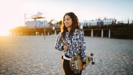 A woman smiling and holding a skateboard on the beach.