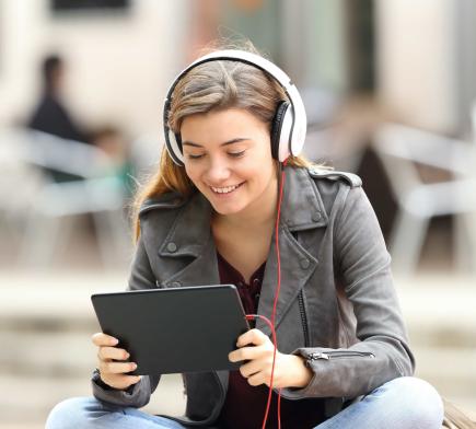 young woman wearing headphones and smiling at a tablet. 